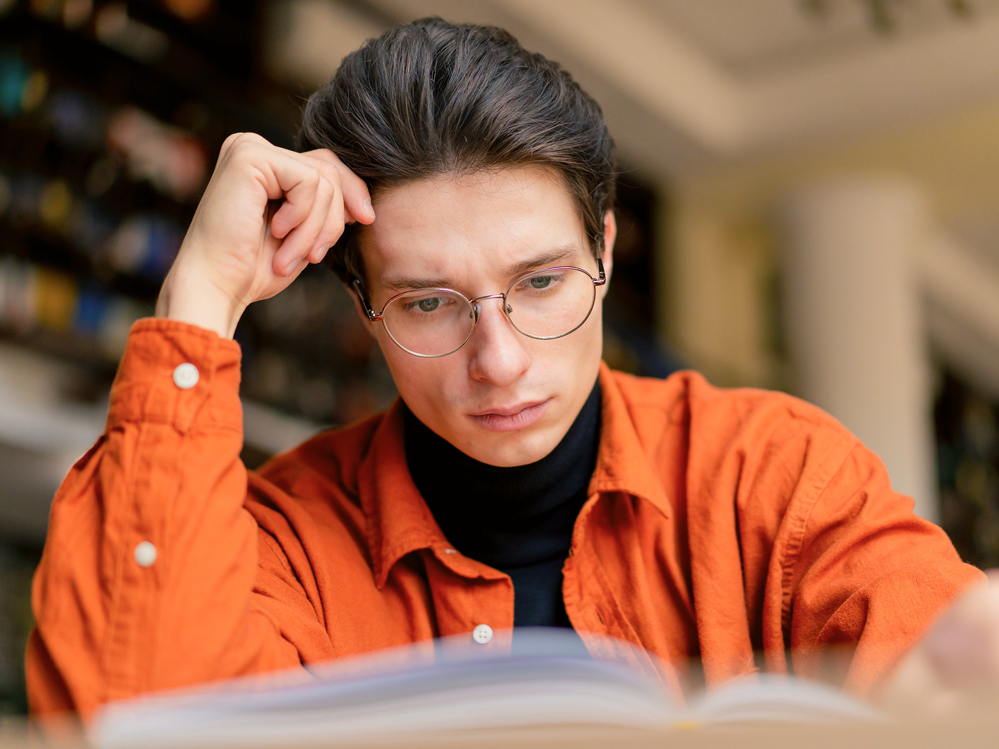 A young man in glasses and an orange shirt looking intently into an open book