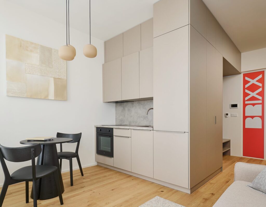 A furnished kitchenette with a small dining table and a red panel with the BRIXX lettering