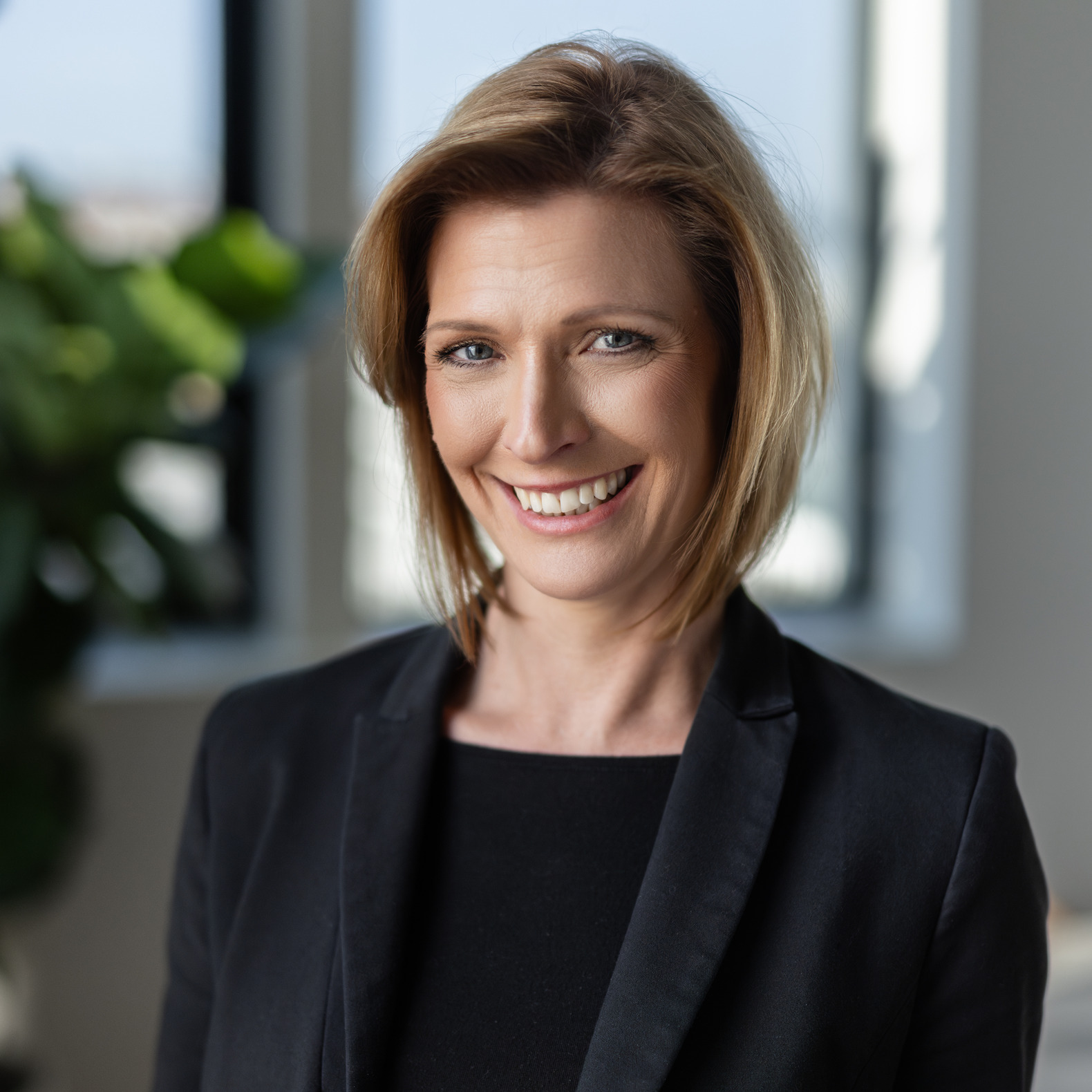 Portrait of a smiling blonde woman in a black blazer in a bright office
