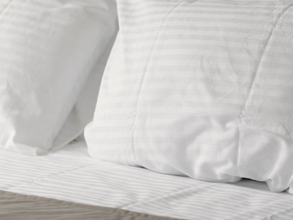 Close-up of white bedding with a fine stripe and pillows on a bed