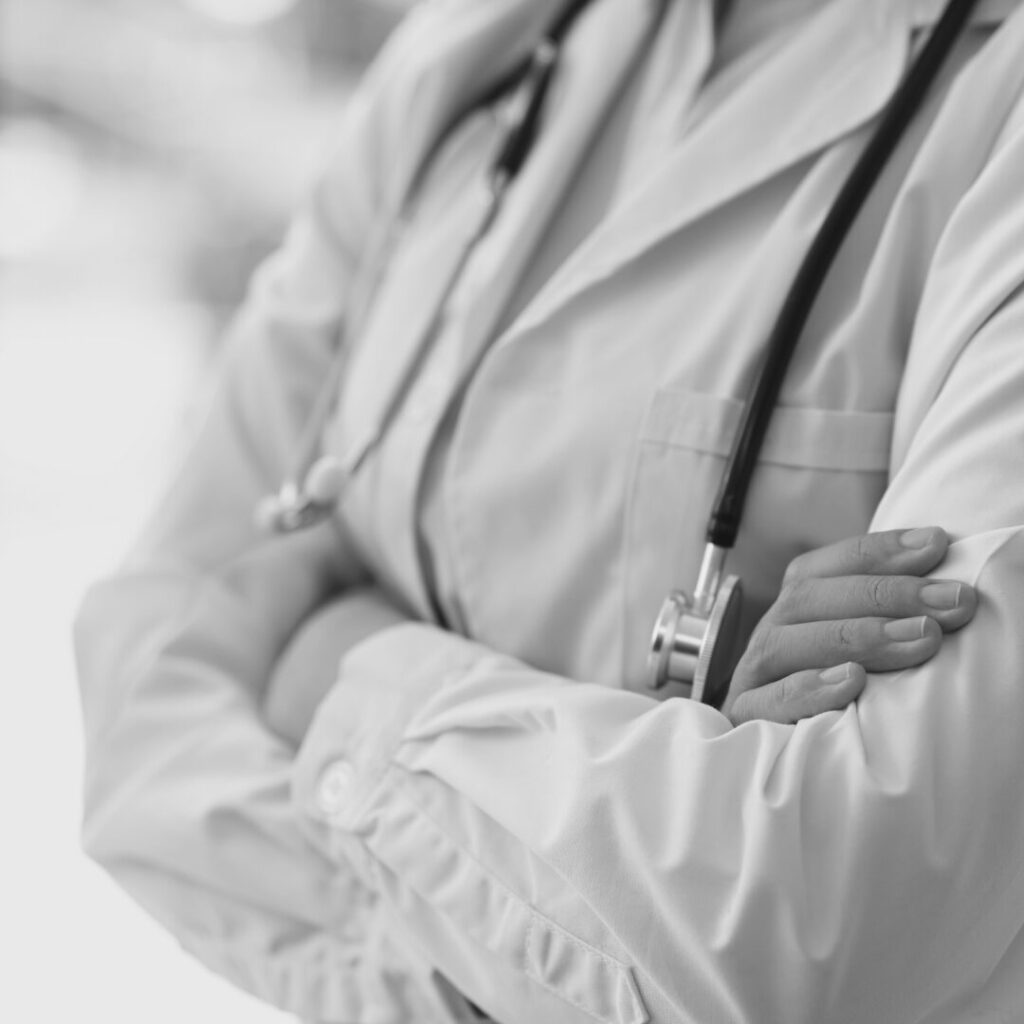 Black and white close-up of a doctor in a white coat with a stethoscope and folded arms