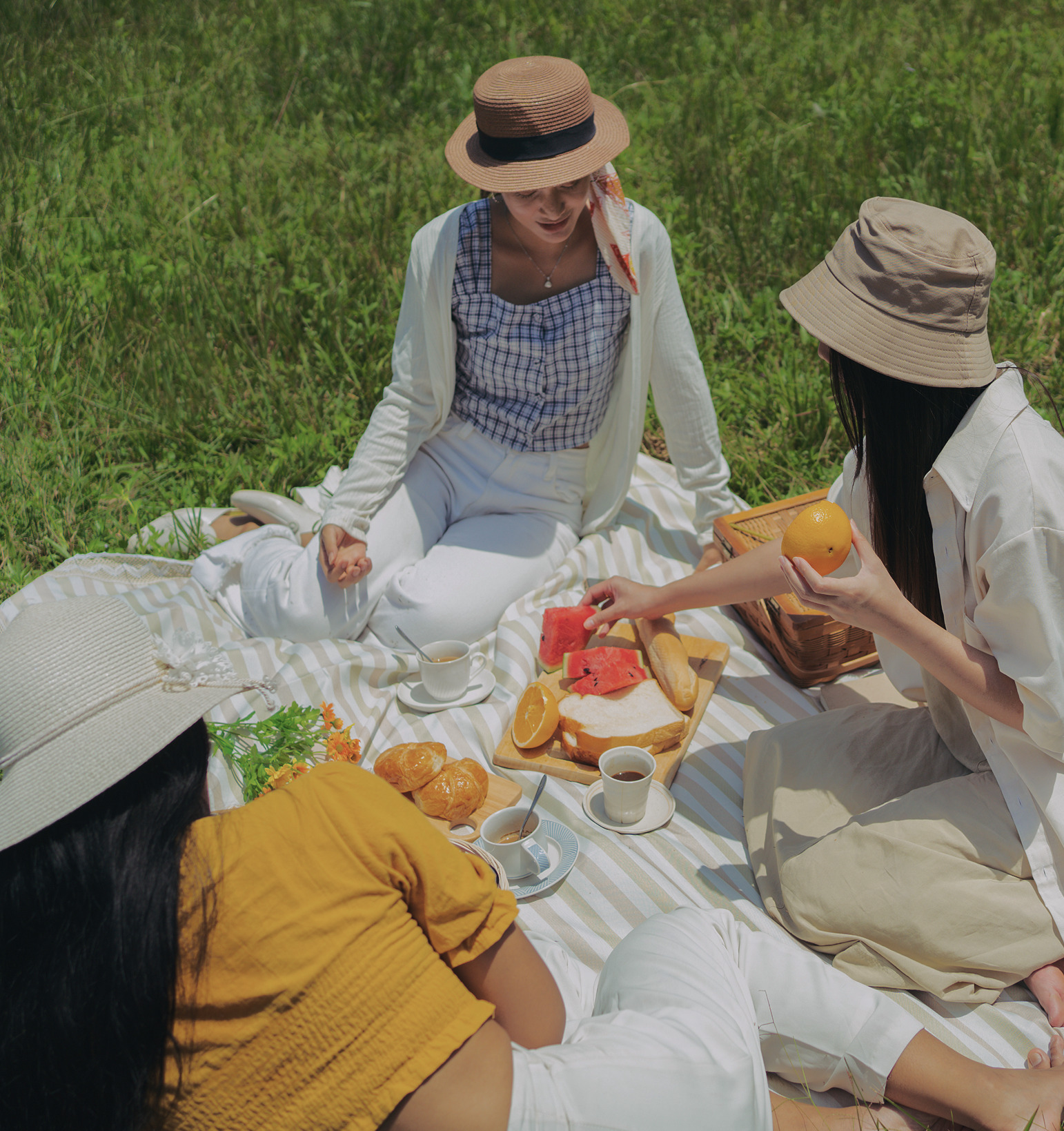 A group of young people at a summer picnic on the grass with fruit, pastries and coffee
