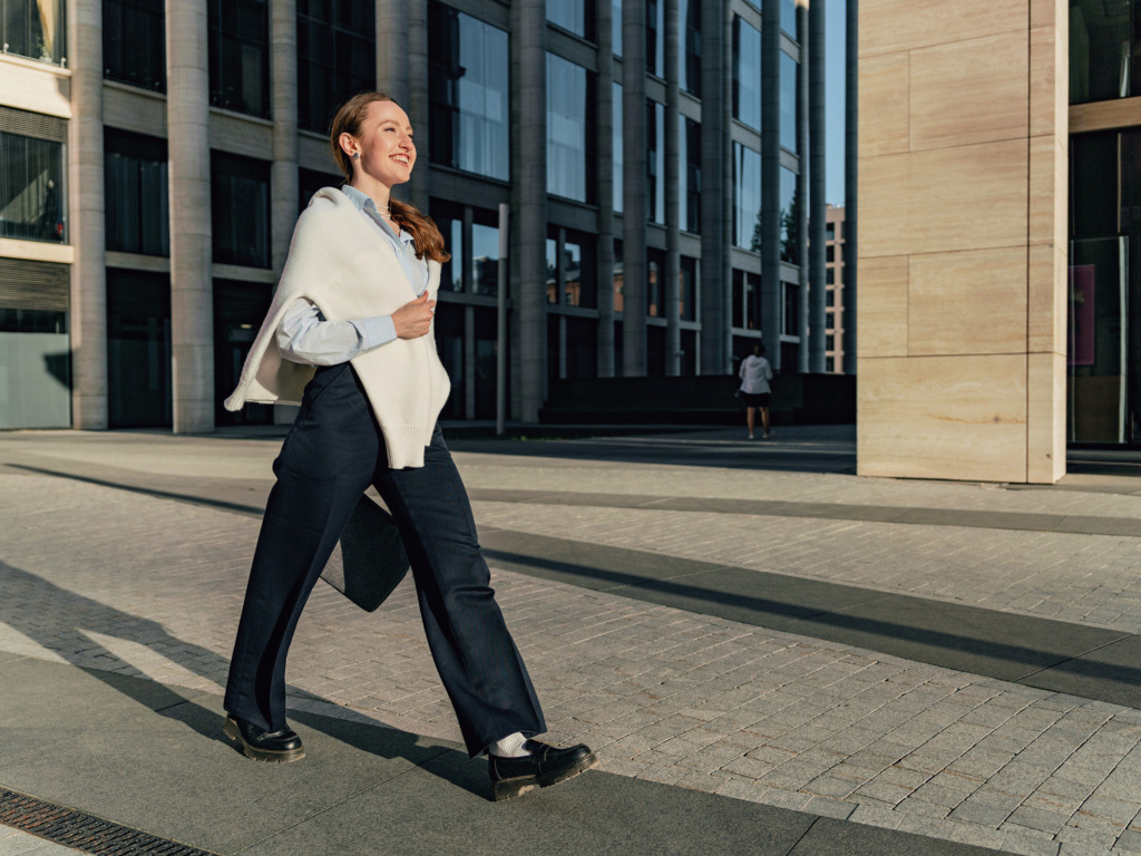 A smiling woman walking across a paved square in front of a modern office building